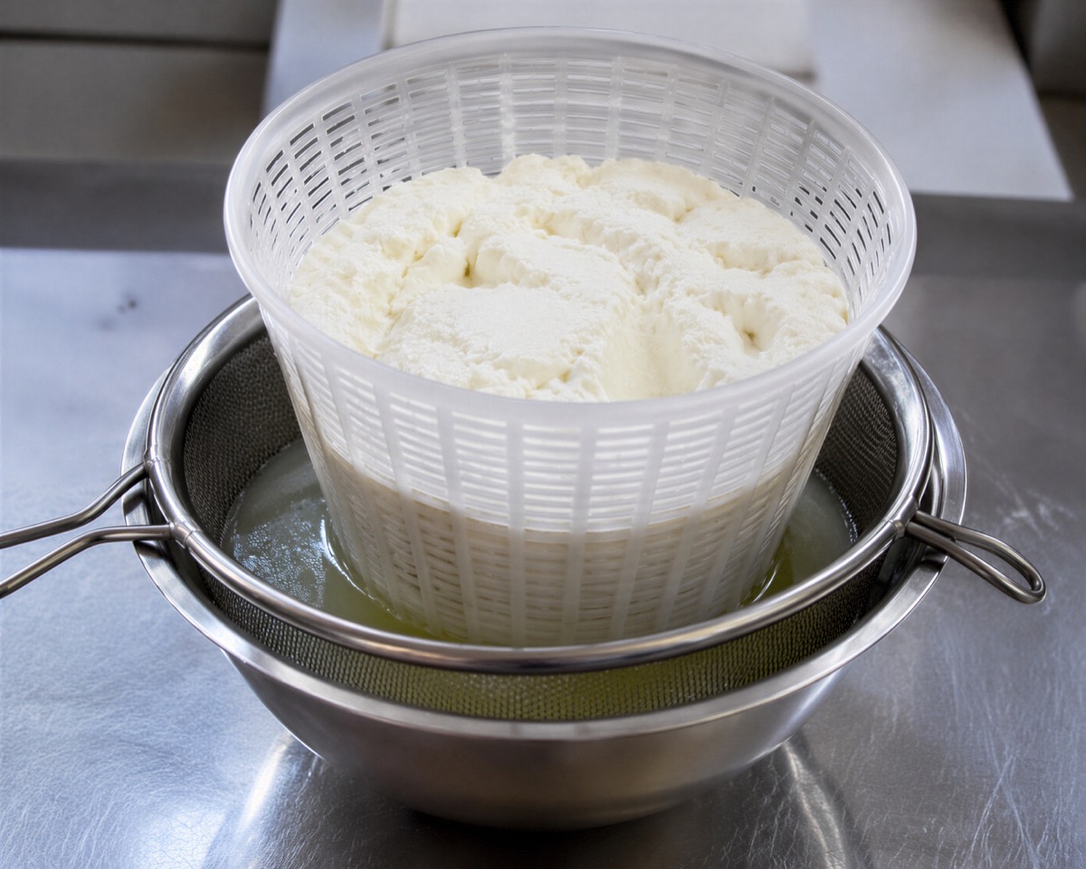 Čerstvá ricotta odkapávající v&nbsp;děrovaném košíku nad syrovátkou